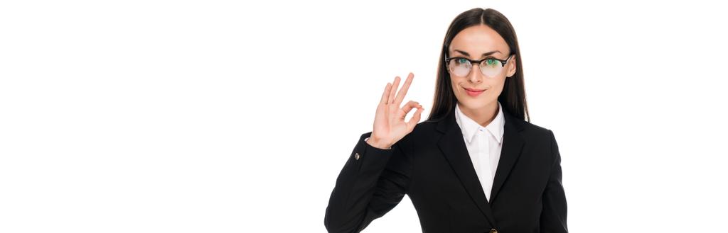усміхнена бізнес-леді в чорному костюмі, що показує знак ОК ізольовано на білому, панорамний знімок
 - Фото, зображення