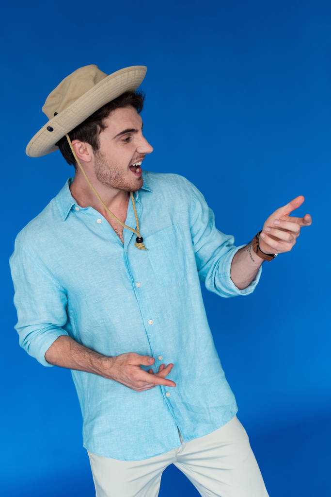 viajero sonriente en safari sombrero gesto y mirando hacia otro lado aislado en azul
 - Foto, imagen