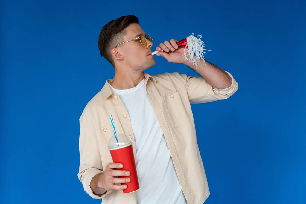 güneş gözlüğü elinde içecek ve parti boynuzu mavi izole adam - Fotoğraf, Görsel