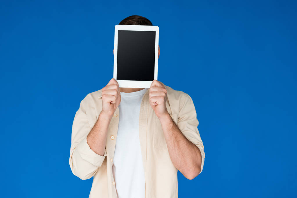 青で隔離された空白の画面を持つデジタルタブレットを保持するシャツの若い男の正面図 - 写真・画像