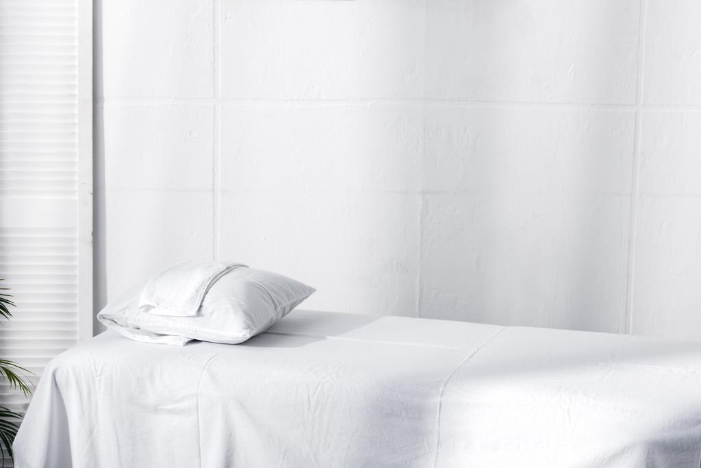 Mesa de masaje con sábana blanca, almohada y toalla en la clínica
 - Foto, imagen