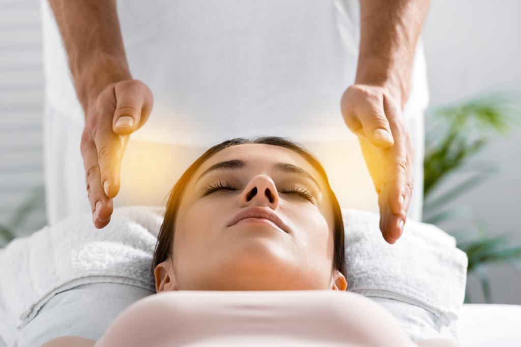 vista cortada de curandeiro em pé perto do paciente na mesa de massagem e limpeza aura
 - Foto, Imagem