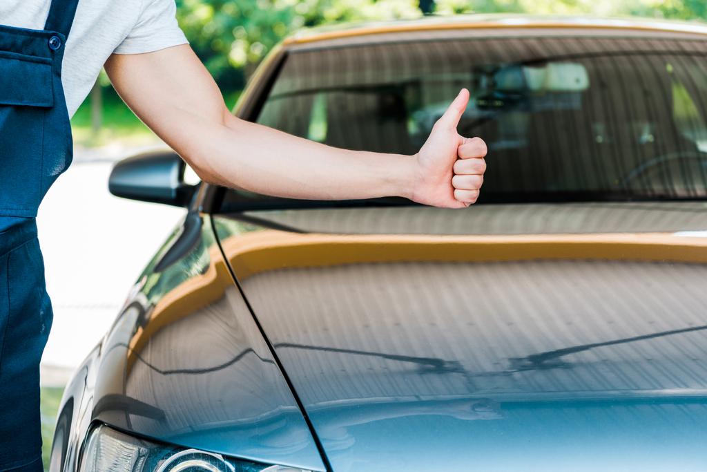 oříznutý pohled na myčku auta ukazující palec nahoře poblíž šedého auta  - Fotografie, Obrázek