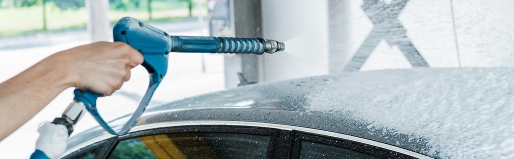 plan panoramique de laveuse de voiture tenant laveuse de pression avec mousse près de la voiture
  - Photo, image