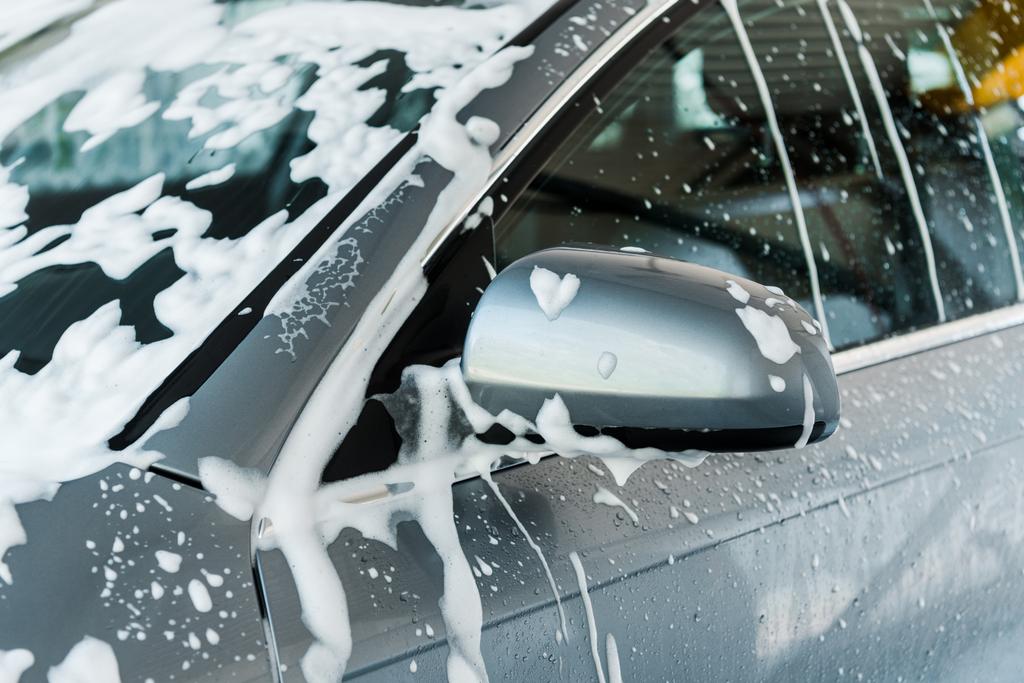 bijgesneden beeld van auto spiegel met wit schuim in carwash  - Foto, afbeelding