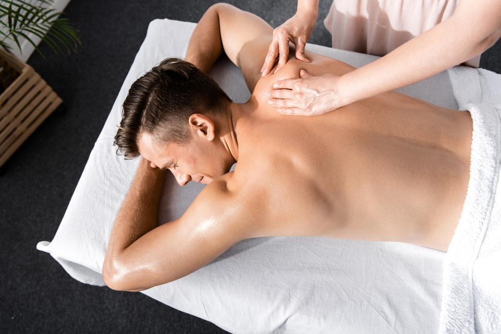 обрізаний вид масажиста і без сорочки чоловік лежить на масажному столі
 - Фото, зображення