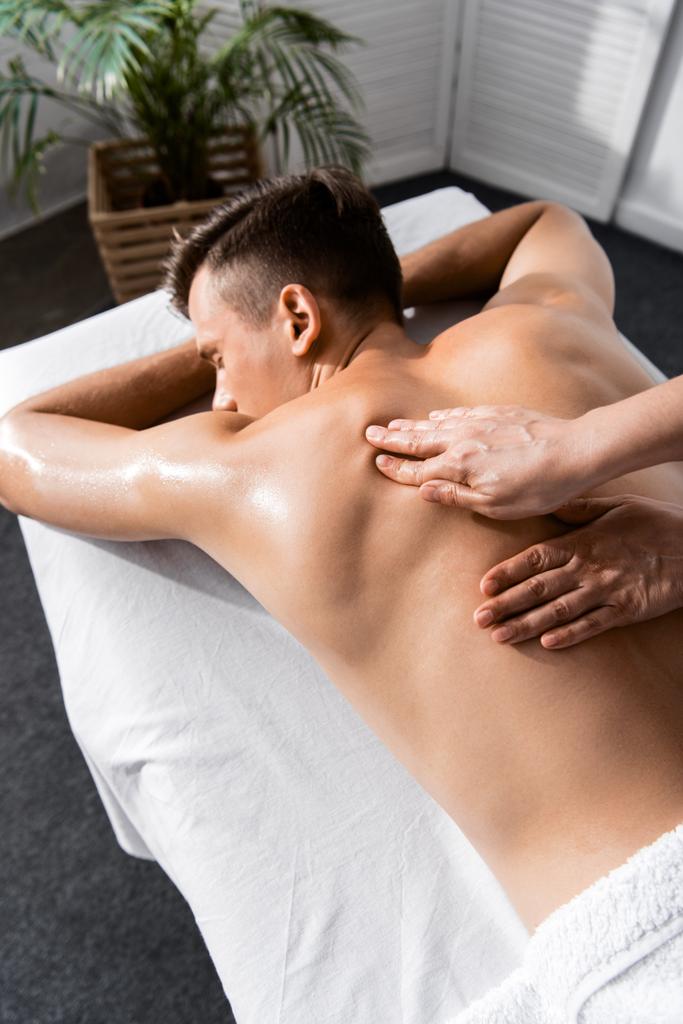vista ritagliata di massaggiatore e uomo senza maglietta sdraiato sul tavolo da massaggio
 - Foto, immagini