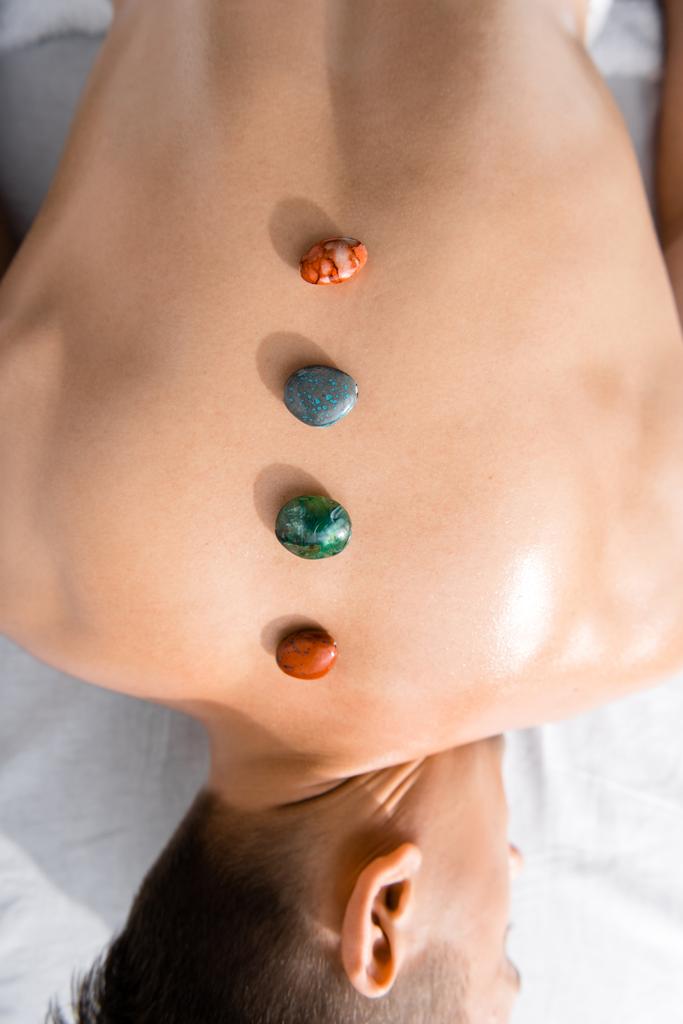 vista recortada del hombre sin camisa acostado en la mesa de masaje con piedras en la espalda
 - Foto, imagen