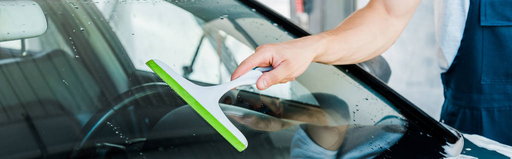 panoramic shot of car washer holding squeegee while cleaning car window  - Photo, Image
