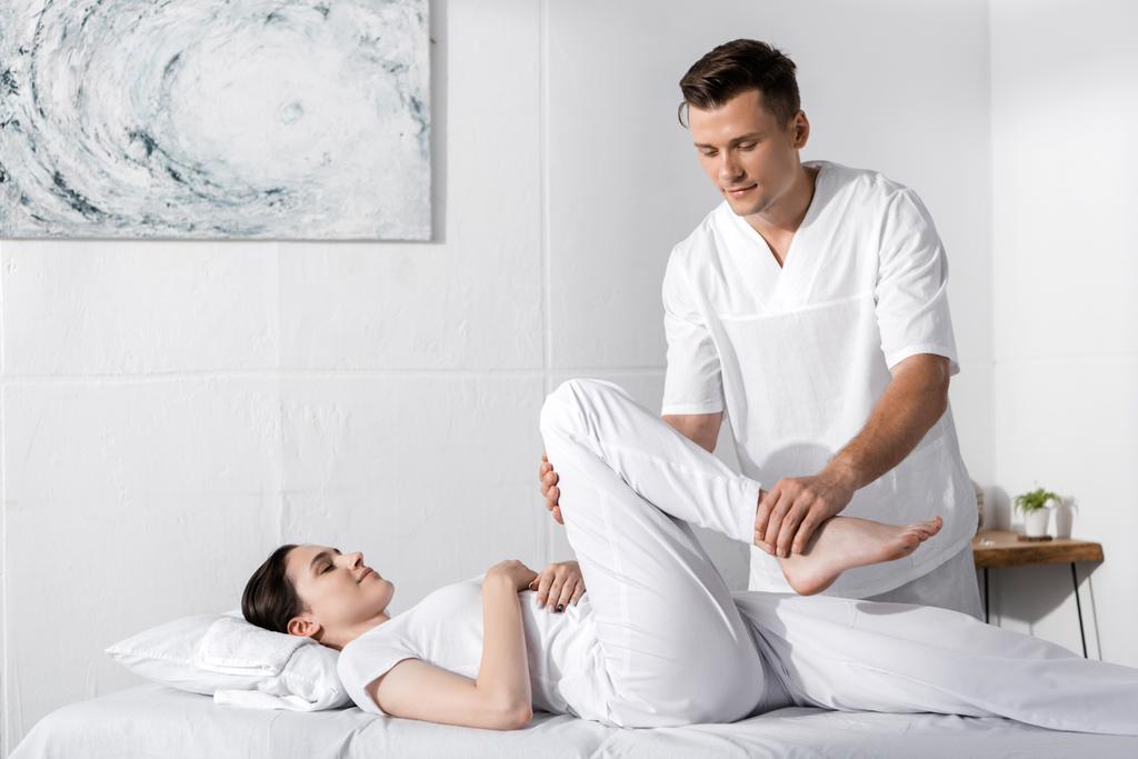 skoncentrowany masażysta stoi blisko kobiety i dotykając jej nogi - Zdjęcie, obraz