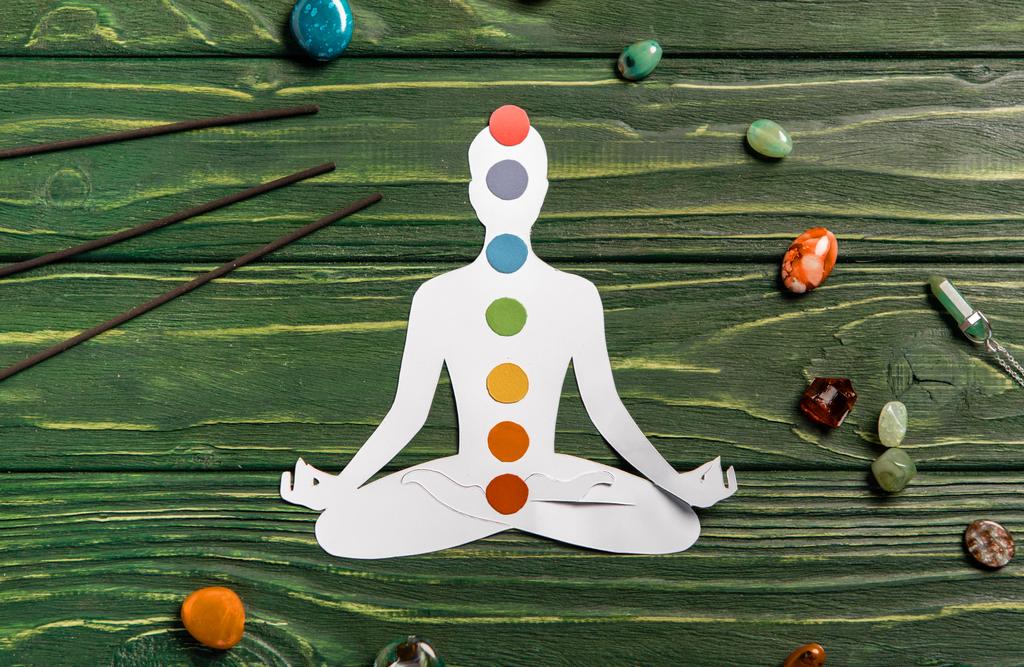 top view of paper figure in form of person with chakras in lotus pose, aroma sticks and colorful stones on wooden surface - Photo, Image