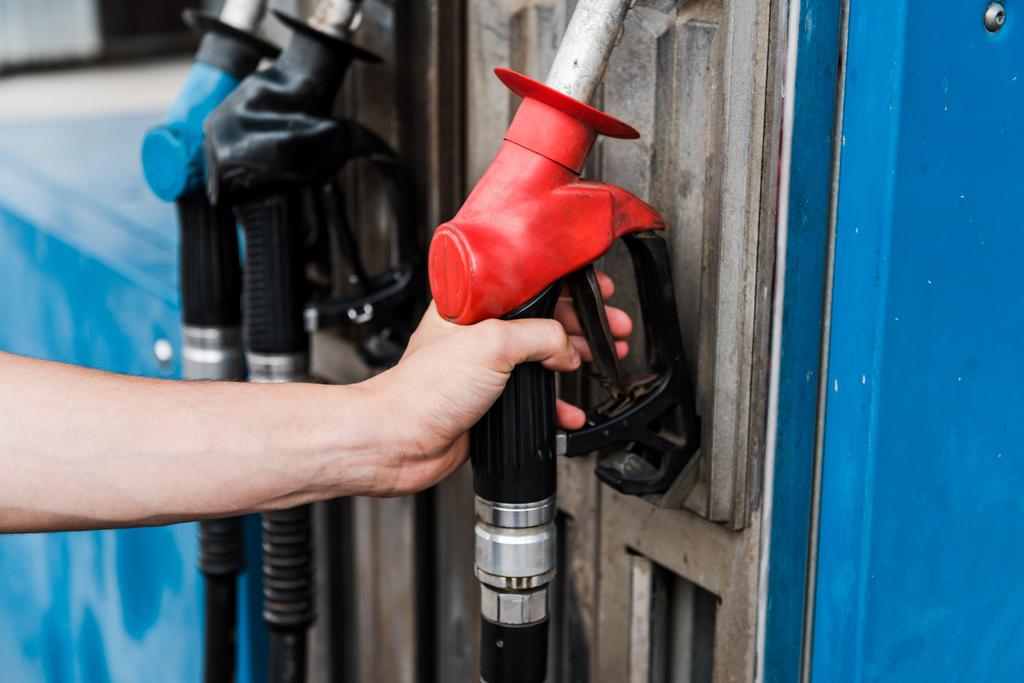 benzin istasyonunda kırmızı gaz pompası tutan adamın seçici odak  - Fotoğraf, Görsel