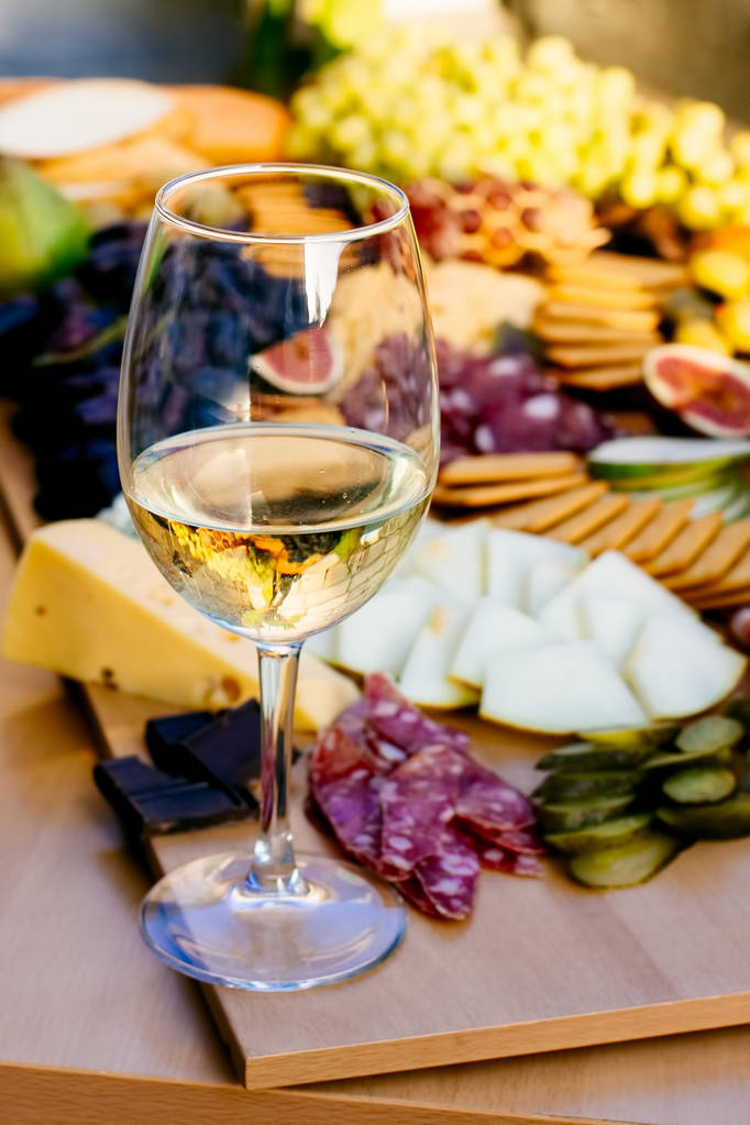 Kuva fantastisesta, kauniista välipaloista, kuten hedelmistä, juustosta, oliiveista, kuivatusta viinilihasta viinipöydällä viinilasilla
 - Valokuva, kuva