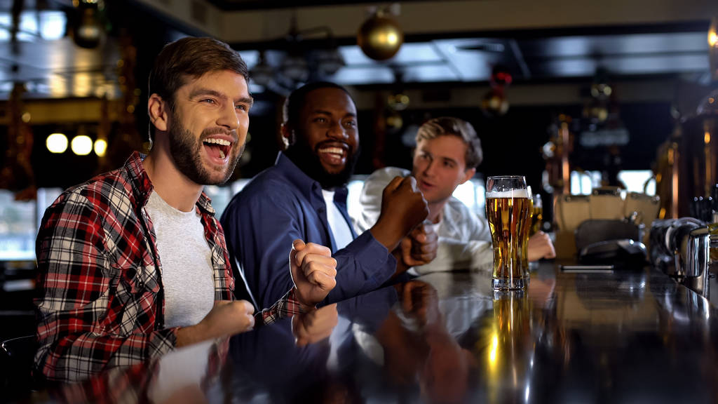 Διαφυλετικός άνδρες φίλοι γιορτάζουν τη νίκη, ζητωκραυγάζουν για την αγαπημένη ομάδα στο μπαρ - Φωτογραφία, εικόνα
