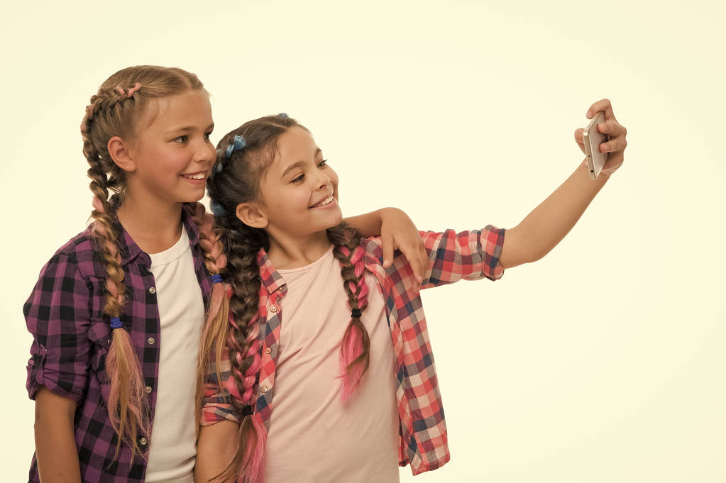 Küçük şirin kızlar telefon ekranına gülümsüyor. Sosyal ağlar için selfie çekmeyi seviyorlar. Genç nesil sorunu. Cep telefonu bağımlılığı. Cep telefonu ve internet bağımlılığı veya saplantı - Fotoğraf, Görsel