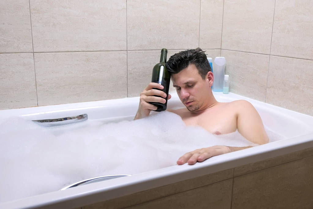 Дорослий втомлений 30-х чоловік спить з пляшкою червоного вина ванни
. - Фото, зображення