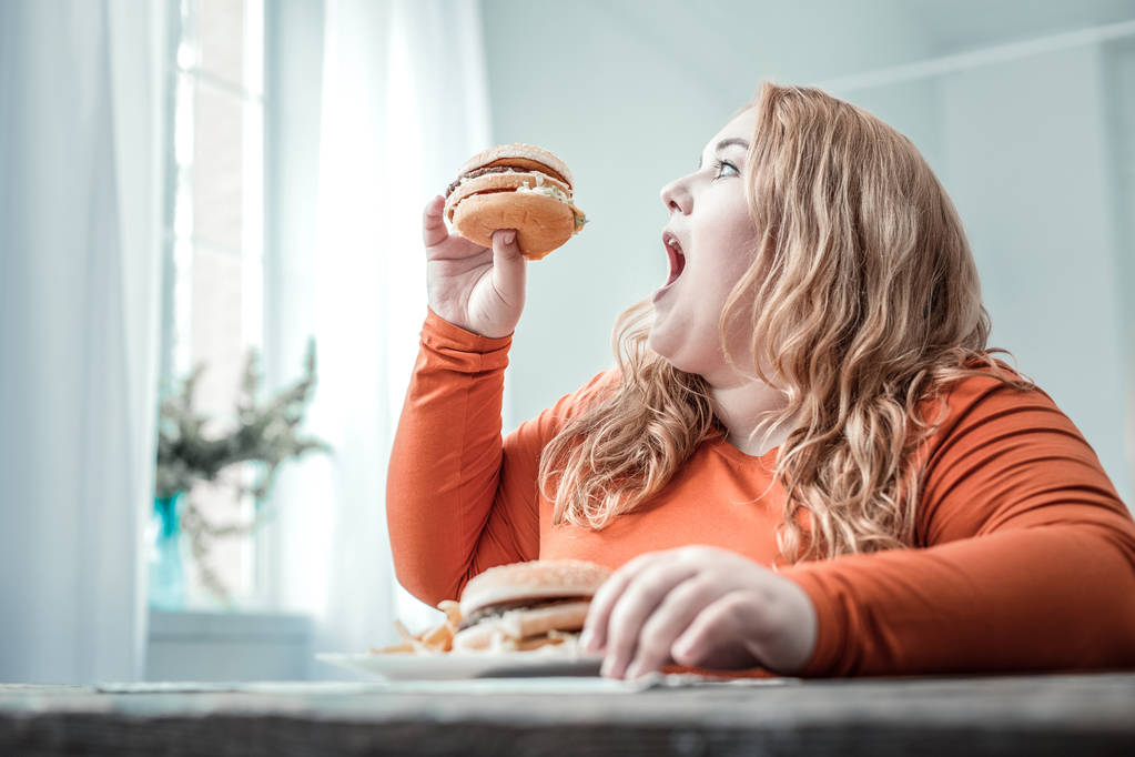 Голодна блондинка пухка жінка їсть нездорову їжу
 - Фото, зображення