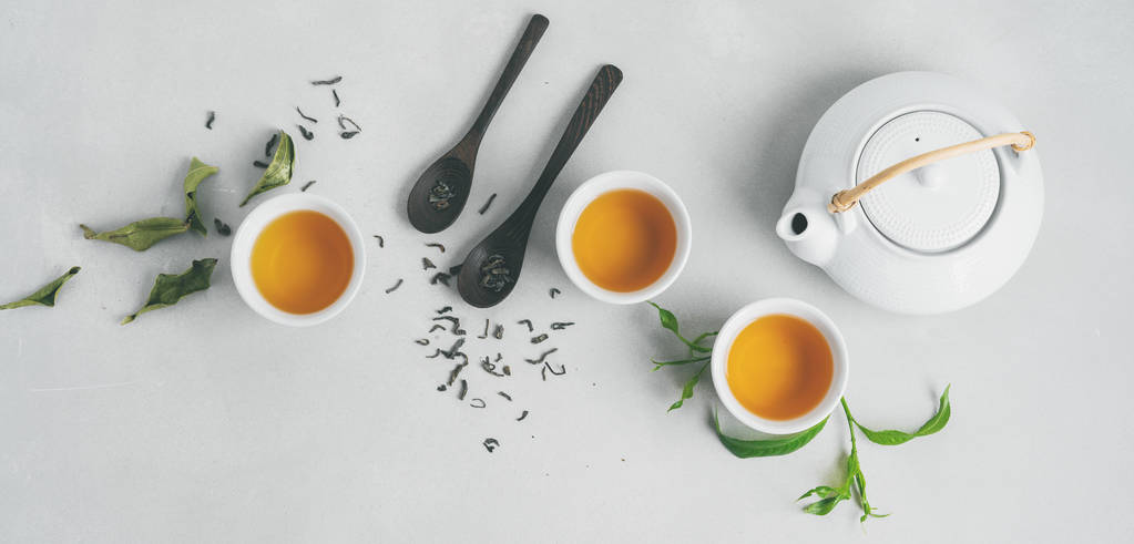 Conjunto asiático com chá verde, xícaras e bule de chá no fundo branco com folhas verdes
  - Foto, Imagem
