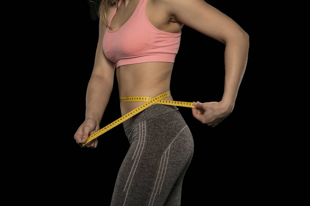 νεαρή γυναίκα με ένα αθλητικό σώμα χρησιμοποιεί μια ταινία μέτρησης - Φωτογραφία, εικόνα