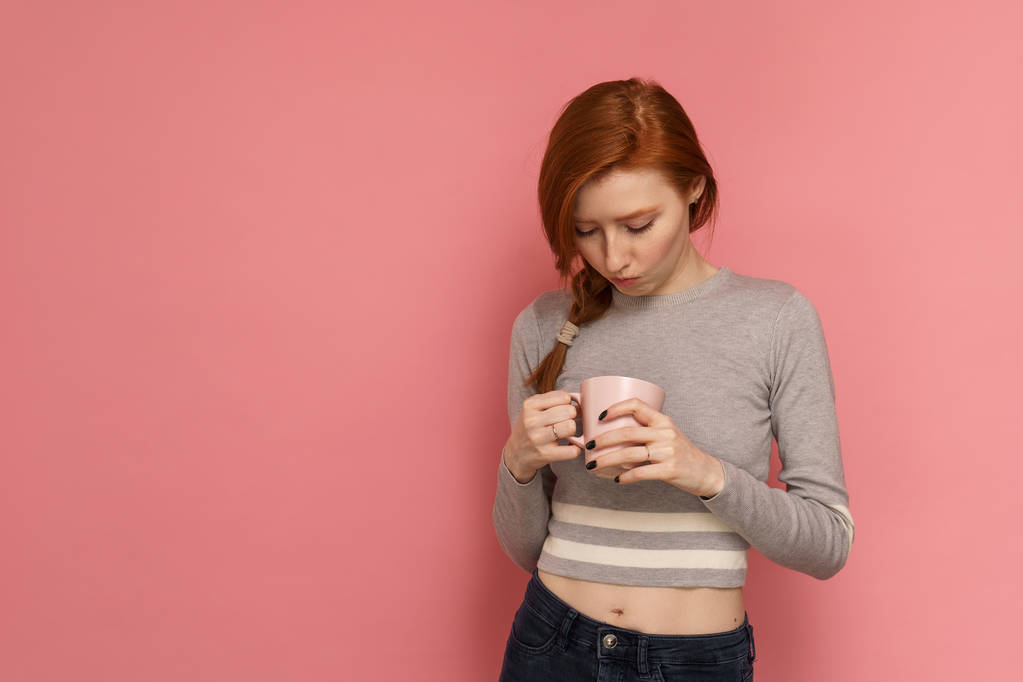 Red-haired girl holds and looking into the cup - Photo, Image