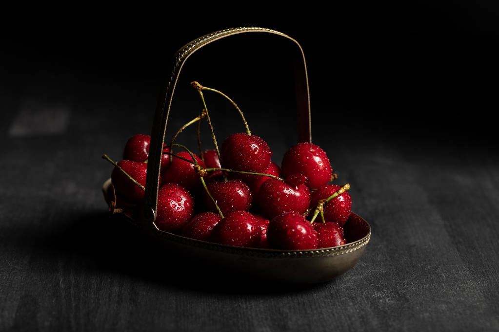 rojo deliciosas cerezas húmedas en cesta de metal sobre mesa oscura de madera aislada en negro
 - Foto, imagen