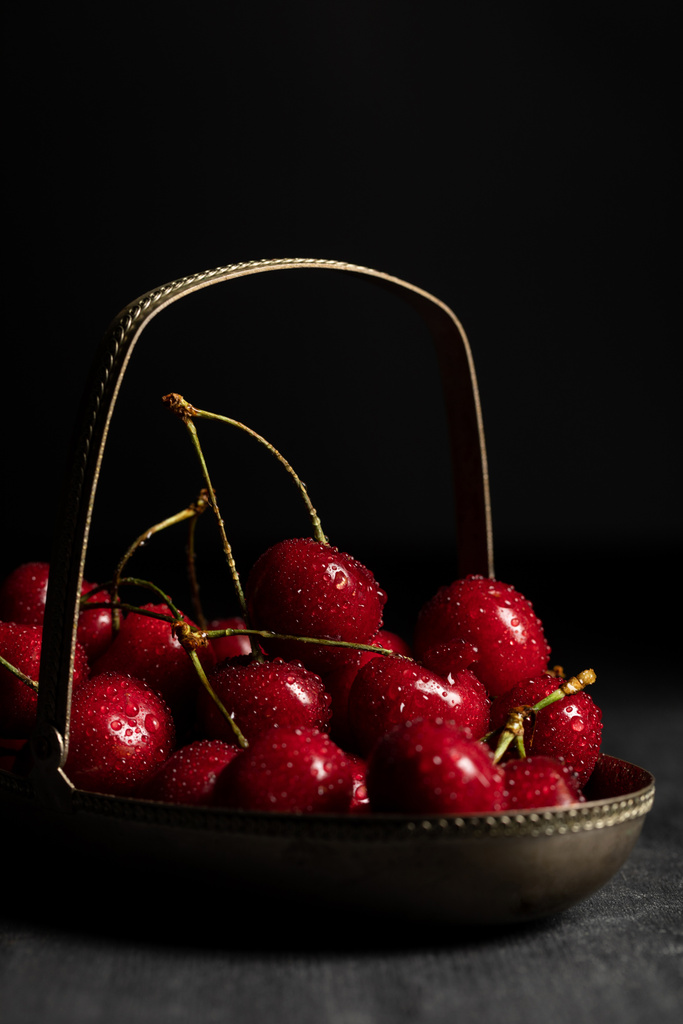 rojo deliciosas cerezas con gotas de agua en cesta de metal sobre mesa oscura de madera aislado en negro
 - Foto, Imagen