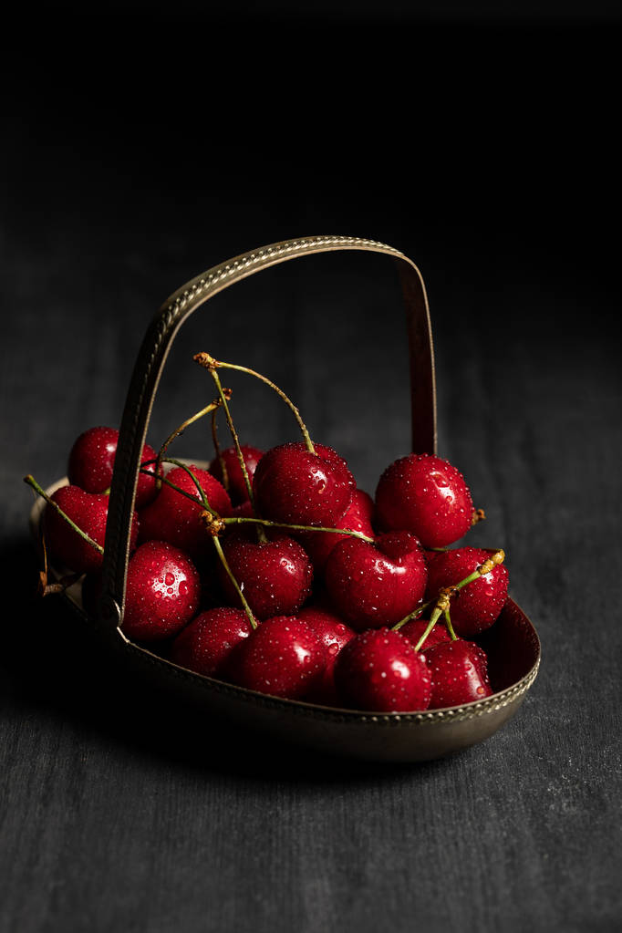 červená chutná, mokré třešně v kovové košíčku na dřevěné tmavé stolovni, izolované na černém - Fotografie, Obrázek