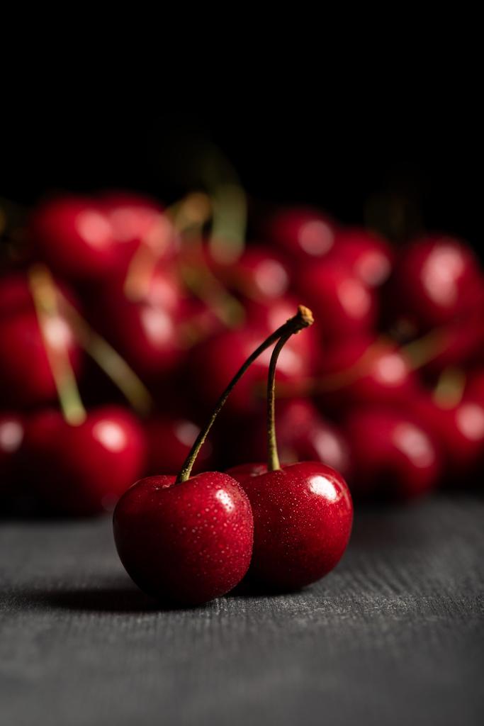 selective focus of red delicious sweet cherries on wooden table isolated on black - Photo, Image
