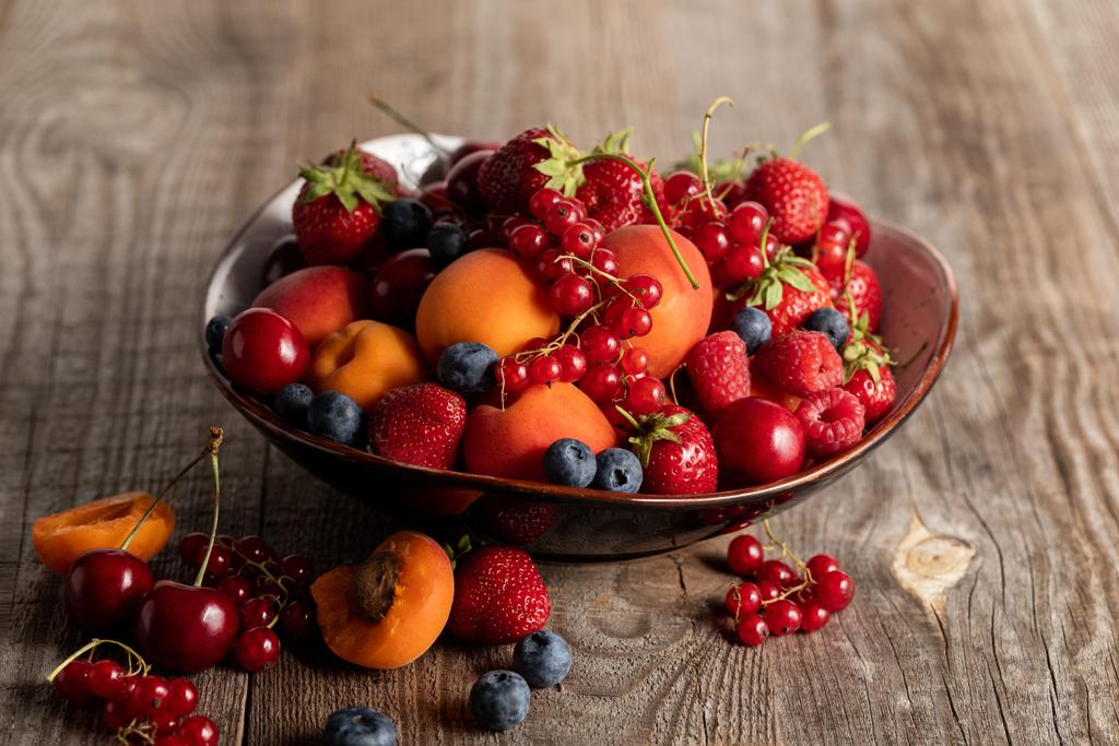 стиглі сезонні ягоди і абрикоси на тарілці на дерев'яному столі
 - Фото, зображення