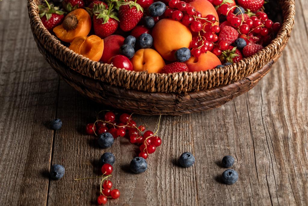 close up view of ripe seasonal berries and apricots in wicker basket on wooden table with copy space - Photo, Image