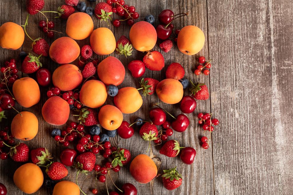верхний вид спелых вкусных сезонных ягод, разбросанных со свежими абрикосами на деревянном столе
  - Фото, изображение