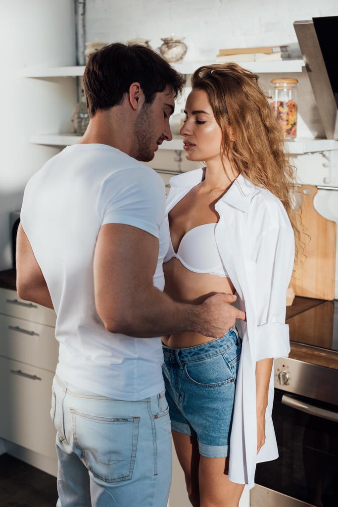 muskularny Człowiek w białym t-shirt obejmując seksowną dziewczynę w kuchni - Zdjęcie, obraz