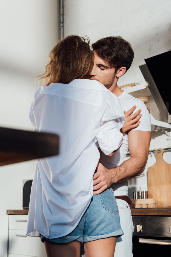 homme musclé embrassant petite amie sexy avec les yeux fermés dans la cuisine
 - Photo, image