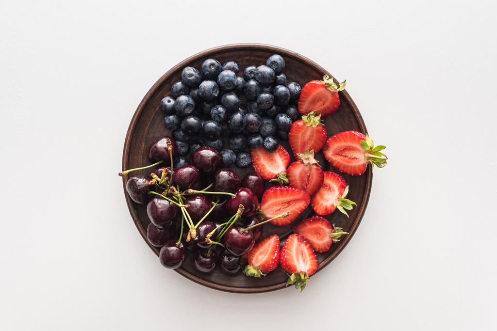 vista dall'alto di mirtilli dolci, ciliegie intere e fragole tagliate sul piatto
  - Foto, immagini