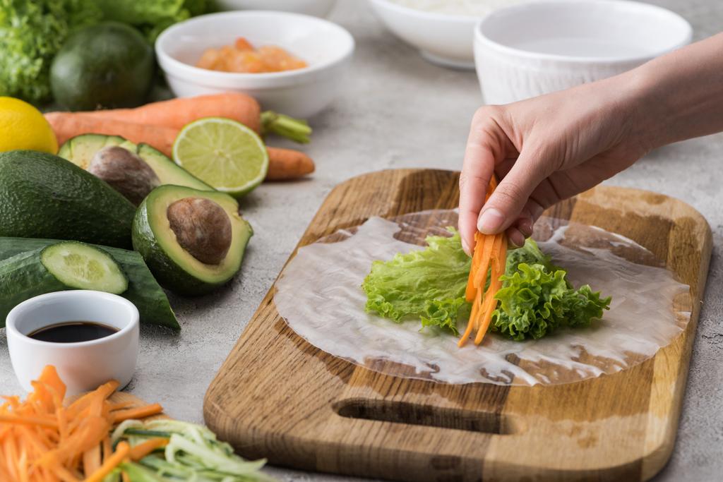 cropped view of woman putting cut carrot on lettuce, on cutting board  - Photo, Image