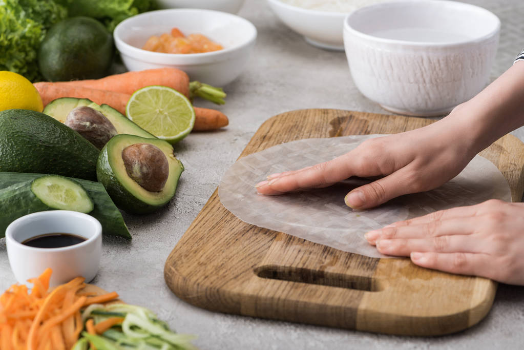 visão cortada da mulher colocando papel de arroz na placa de corte entre os ingredientes
  - Foto, Imagem