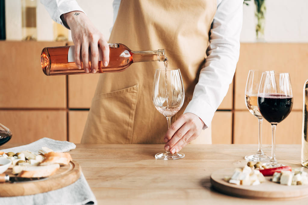 partial view of sommelier in apron holding bottle and pouring wine in wine glass - Photo, Image