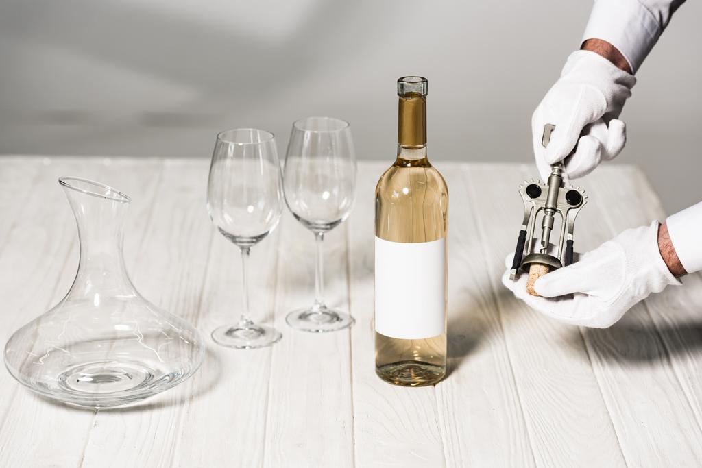 Beyaz eldivenlerde garson kısmi görünümü şişe yakın masada korkvida tutan, şarap gözlükleri ve sürahi - Fotoğraf, Görsel