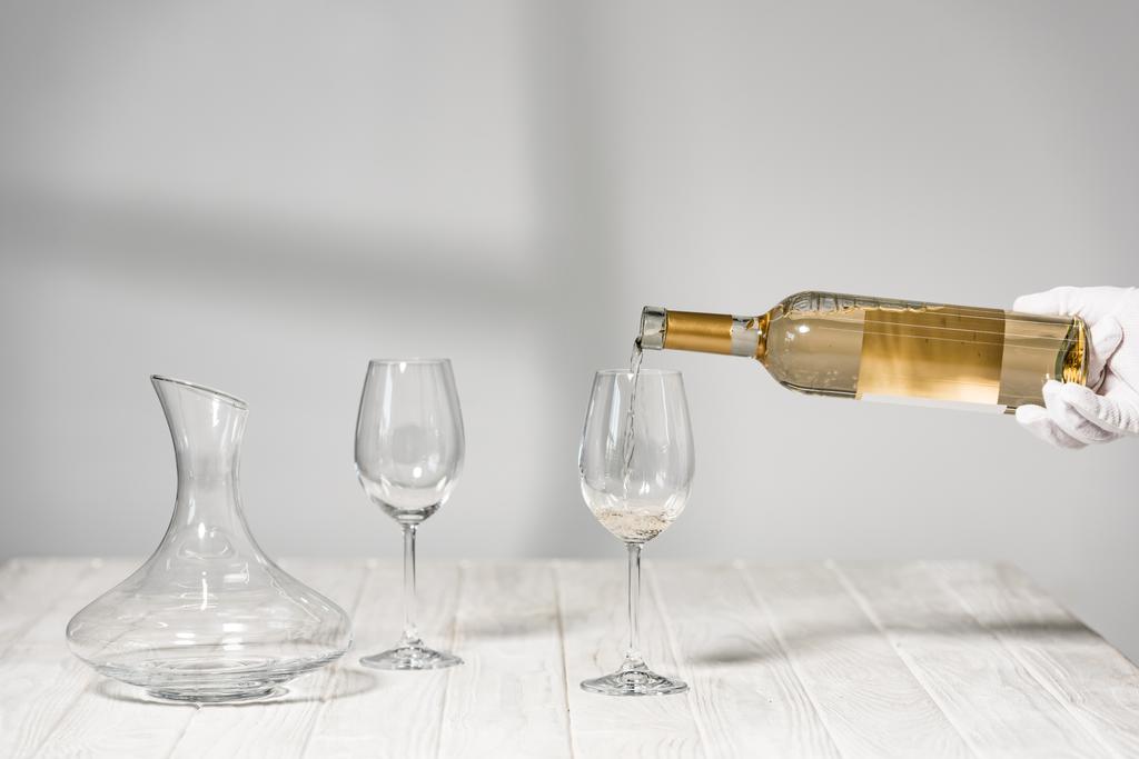 ahşap masada şarap gözlükleri yakın şarap şişe tutan beyaz eldiven su kırpılmış görünümü - Fotoğraf, Görsel