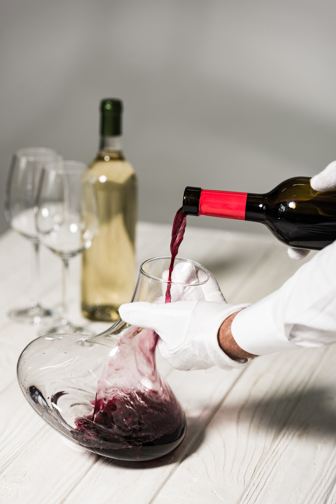 μερική θέα του σερβιτόρου με λευκά γάντια που ρίχνουν κρασί σε κανάτα - Φωτογραφία, εικόνα