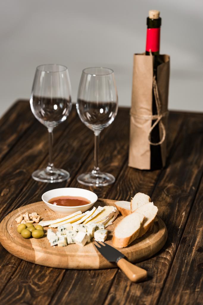 fles wijn, wijn glazen, kaas, olijven, saus en brood op houten oppervlak - Foto, afbeelding