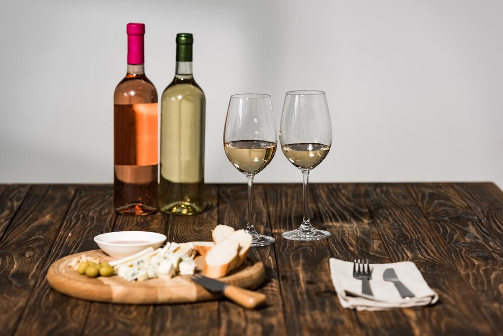 flessen wijn, wijn glazen, bestek, kaas, olijven, saus en brood op houten oppervlak - Foto, afbeelding