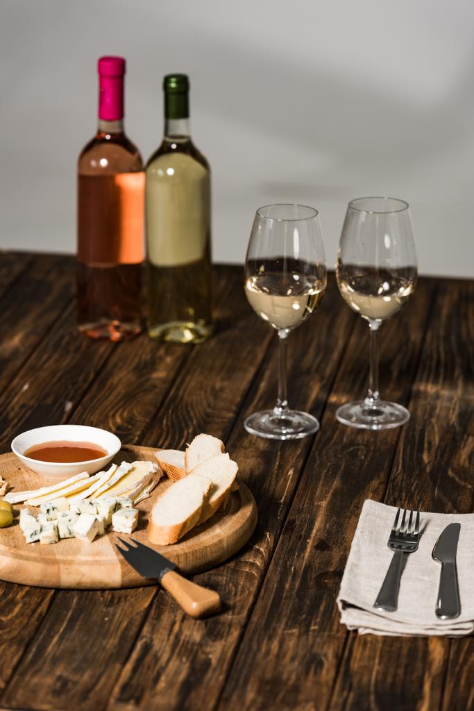 láhve vína, vinné sklenice, příbory, sýry, olivy, omáčky a chléb na dřevěné ploše - Fotografie, Obrázek
