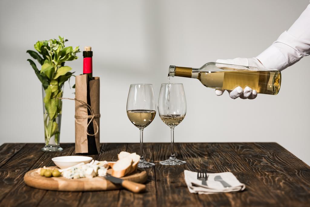 обрезанный вид официанта в белых перчатках, наливающего вино в бокалы
 - Фото, изображение