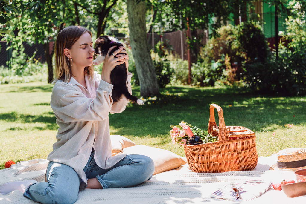 Blond dziewczyna siedzi na kocu w ogrodzie i trzyma szczeniaka w słoneczny dzień - Zdjęcie, obraz