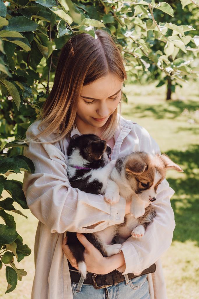 chica rubia sosteniendo lindos cachorros en el jardín cerca de árbol verde
  - Foto, imagen