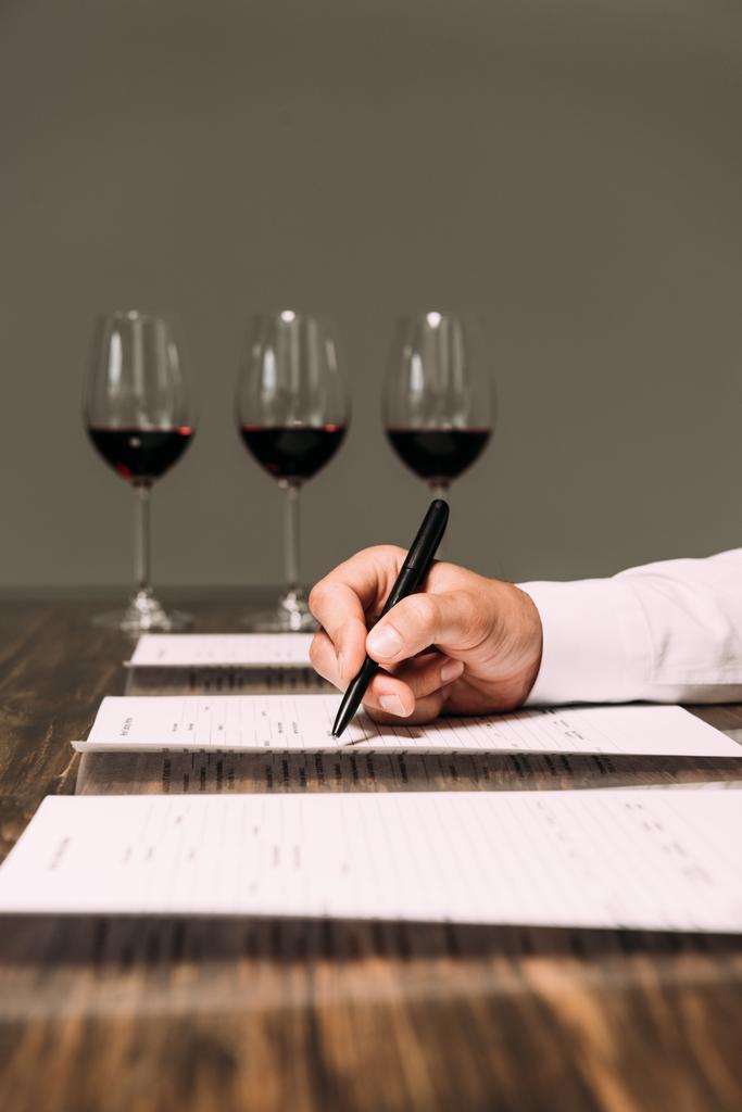 Ausgeschnittene Ansicht eines Sommeliers, der Dokumente am Tisch mit Weingläsern schreibt - Foto, Bild
