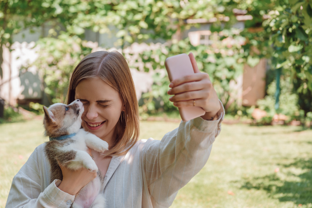 menina loira no jardim verde levando selfie com olhos fechados e filhote de cachorro adorável
 - Foto, Imagem
