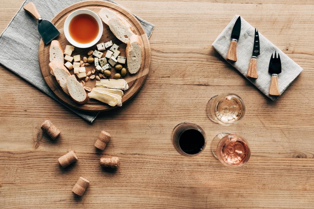 pohled na vinné sklenice, omáčky, chléb, sýr, olivy, korky a kuchyňské náčiní na dřevěném povrchu - Fotografie, Obrázek