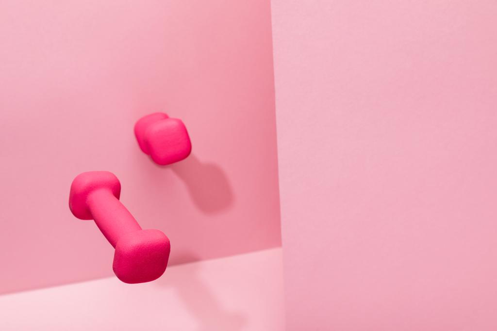 pink bright dumbbells flying in air on pink background with copy space - Photo, Image